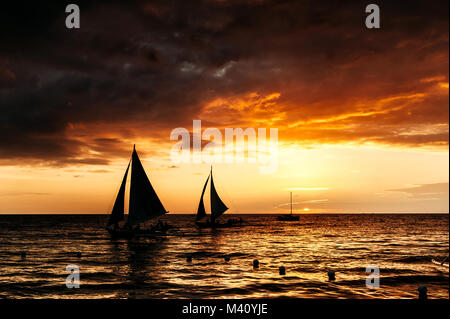 Dramatic orange sea sunset with sailboat in tropical country, clouds. Wide angle. silhouettes of boats, the solar disk. Philippines, Boracay Stock Photo