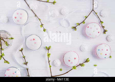 Top view Easter holiday composition of branches with young shoots of greenery, decorated cupcakes, merengue sweets, ribbon and colored bird figure on  Stock Photo