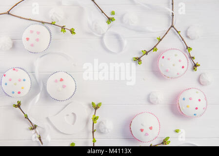 Top view Easter holiday composition of branches with young shoots of greenery, decorated cupcakes, merengue sweets, ribbon and colored bird figure on  Stock Photo