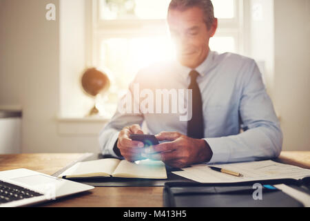 Mature businessman sending text messages on his cellphone while sitting at his desk in an office Stock Photo
