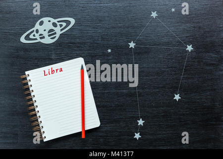 Zodiacal star, constellations Libra on a black background with a notepad and pencil. Stock Photo