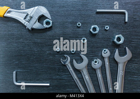 Spanners of different sizes lie with nuts on a black wooden table. Spanners. Stock Photo