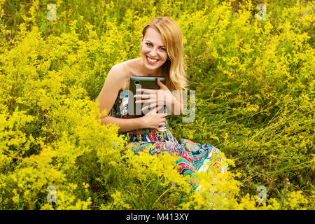 Girl with a black tablet in the field. Girl in a field with a tablet. Stock Photo