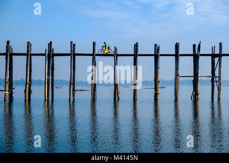 A cyclist is riding on U Bein Bridge, an old teakwood bridge, spanning over Taungthaman Lake Stock Photo