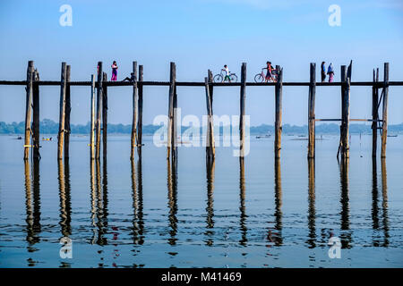 People and cyclists are walking on U Bein Bridge, an old teakwood bridge, spanning over Taungthaman Lake Stock Photo