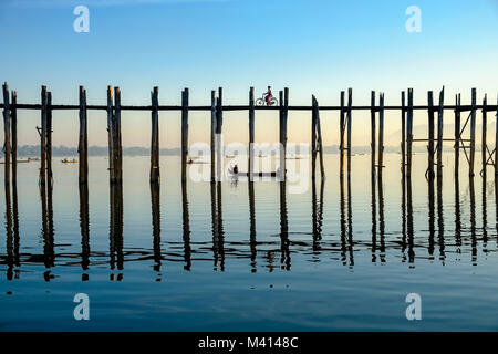 A cyclist is riding on U Bein Bridge, an old teakwood bridge, spanning over Taungthaman Lake Stock Photo