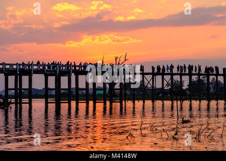 Many people are walking on U Bein Bridge, an old teakwood bridge, spanning over Taungthaman Lake, at sunset Stock Photo