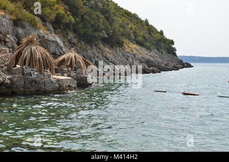 Straw parasols on beach rocks with green sea water in summer Stock Photo