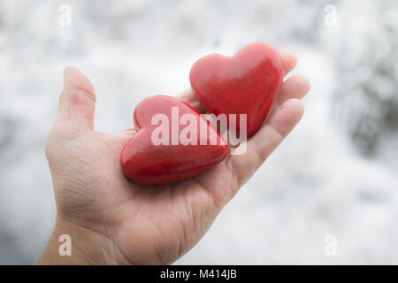 Two red painted hearth shaped figurines on man's palm with snow in the background Stock Photo
