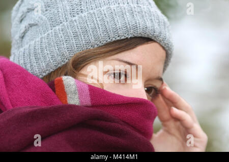 portrait of a young woman on a cold winter day, with woolen cap and pink scarf drawn up Stock Photo