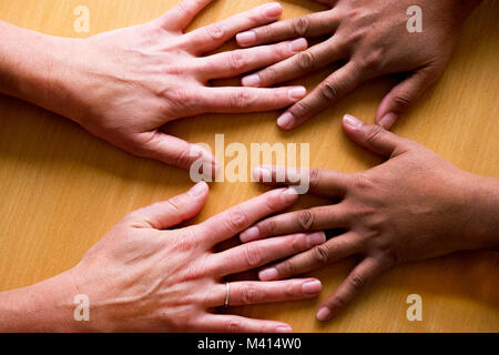 looking down on four fifty year old female hands spread out, lying flat on a table, the two hands on the left a Asian hands and the two on the right a Stock Photo
