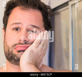 A young adult Caucasian male has his hand on his cheek as he hesitates to get ready for work. Stock Photo