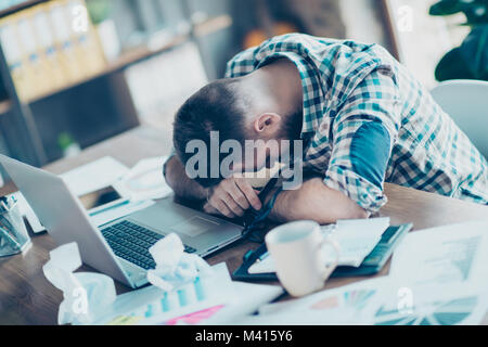 Concept of having no idea and inspiration. Tired confused exhausted sleepy worker is leaning on desktop in front of computer screen and surrounded by  Stock Photo