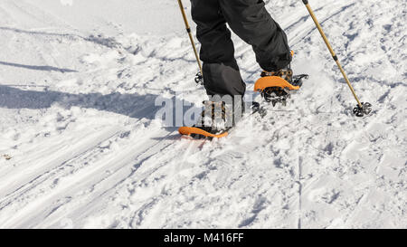 Man with orange snowshoe on the snow path. Man in snowshoes with trekking poles is the snow in the mountains. Snowshoe is most versatile and highest-p Stock Photo