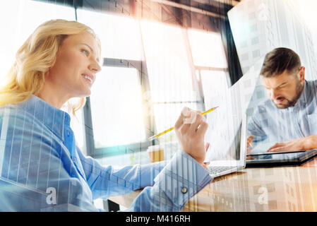 Cheerful woman checking the documents while her colleague working near Stock Photo