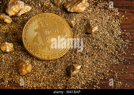 Golden Bitcoin coin on sand mound with golden nuggets Stock Photo