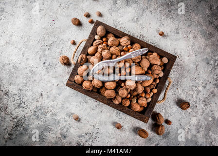 Various nuts and nutcracker in wooden box. On rustic grey stone table, copy space Stock Photo