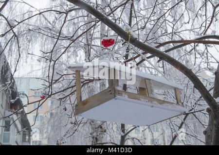 Wooden feeding trough for birds hanging on the tree of Rowan, covered with snow Stock Photo