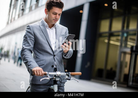 Businessman cycling to work using smartphone Stock Photo