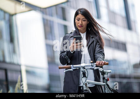 Businesswoman cycling to work using smartphone Stock Photo