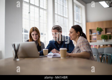 Coworkers looking at a laptop in a meeting Stock Photo