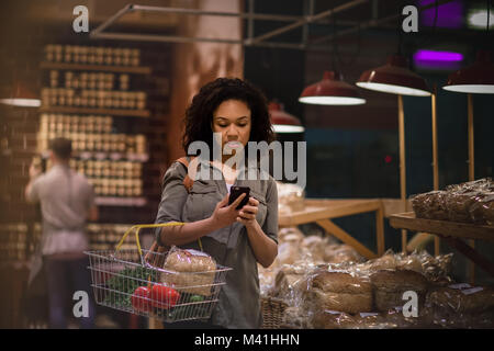Woman late night grocery shopping and using smartphone Stock Photo