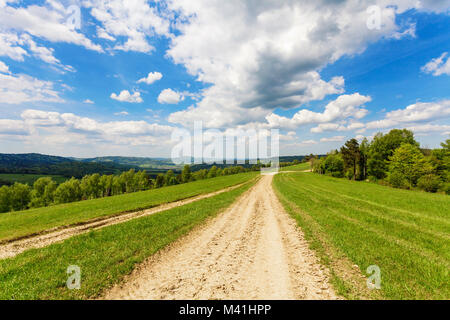 Blue cloudy sky over green hills and country road Stock Photo