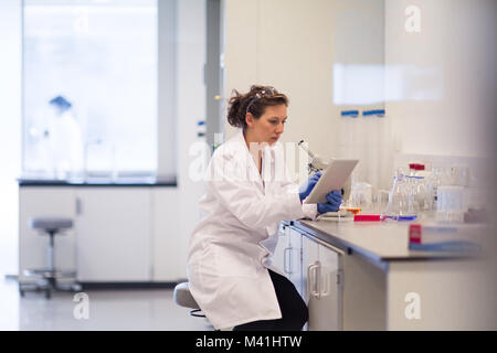 Female scientist looking at results of experiment on digital tablet Stock Photo