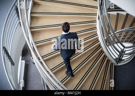Businessman walking up spiral staircase in office Stock Photo