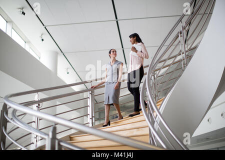 Female business colleagues walking down spiral staircase Stock Photo