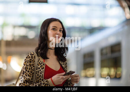 Young adult female on station platform using smartphone Stock Photo