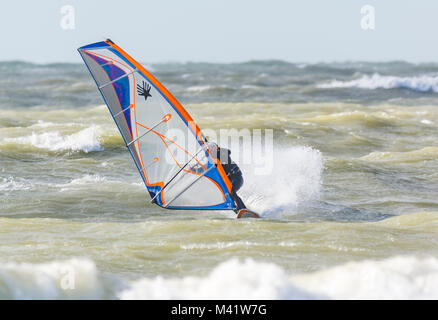Man windsurfing (AKA sailboarding) on a rough sea on a windy day in England, UK. Male windsurfer. Stock Photo