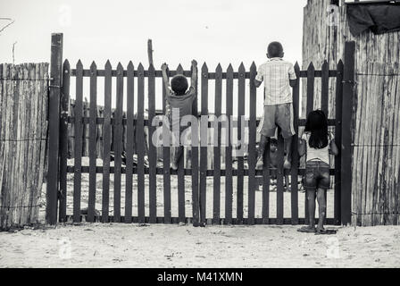 Black and white photo of 3 children climbing up and looking over a wooden gate Stock Photo