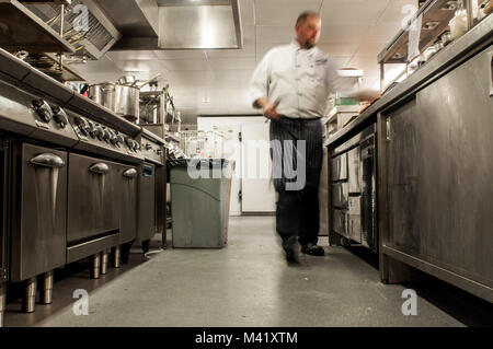 A photo with motion blur of a chef moving quickly in a restaurant kitchen Stock Photo