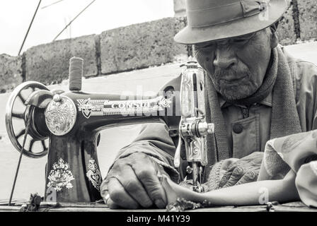 An elderly man making an expression of concentration while using a sewing machine Stock Photo