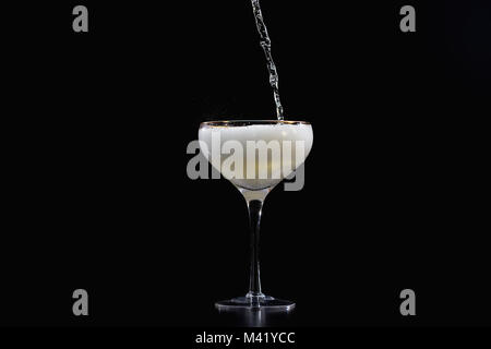 Pouring champagne sparkling wine into glass with black background Stock Photo