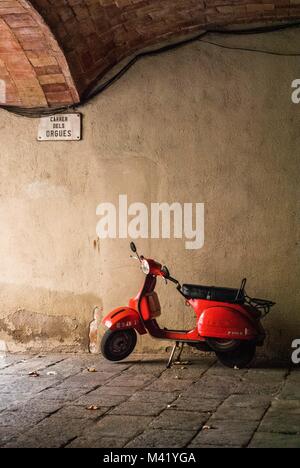 An old, orange scooter parked under a brick arch on a back street in Barcelona, Spain Stock Photo