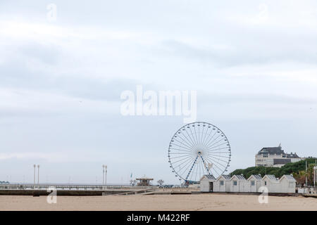 Arcachon ferris wheel on the main pier (Jetee) during a cloudy winter afternoon. The beach and some merchants huts are visible in front. Arcachon is o Stock Photo