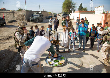 Local Iraqi residents offer homemade food to Iraqi federal police officers and Italian army soldiers assigned to the 3rd Alpine Regiment, deployed in support of Operation Inherent Resolve, during an Italian army and Iraqi school officials during a key leader engagement and civil affairs assessment at a primary school in Aski Mosul, Iraq, Nov. 3, 2017. The breadth and diversity of Coalition partners demonstrates the global and unified goal of defeating ISIS in Iraq and Syria. CJTF-OIR is the global Coalition to defeat ISIS in Iraq and Syria. (U.S. Army photo by Sgt. Tracy McKithern) Stock Photo
