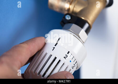 Person's Hand Adjusting Temperature On Thermostat To Control Heat In Central Heating System Stock Photo