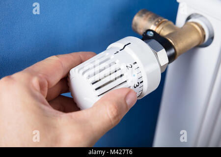 Person's Hand Adjusting Temperature On Thermostat To Control Heat In Central Heating System Stock Photo