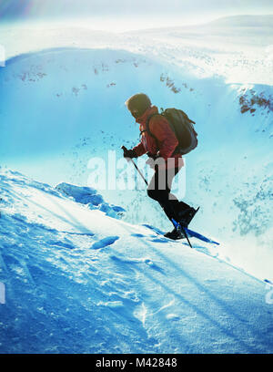 The man with snowshoes on his feet rises to the top. Man with snowshoe on the snow path. Man in snowshoes with trekking poles is the snow in the mount Stock Photo