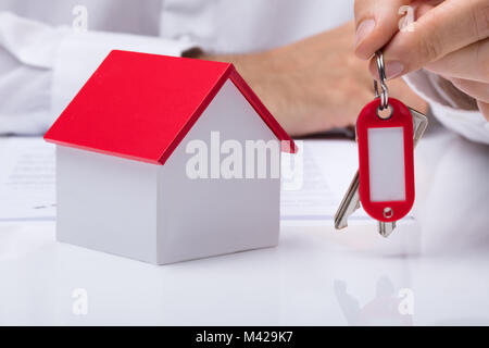 Human Hand Holding House Keys With House Model On Desk Stock Photo