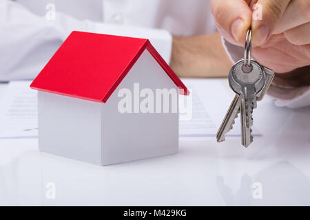 Human Hand Holding House Keys With House Model On Desk Stock Photo