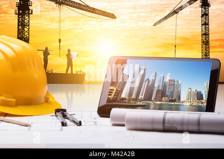Close-up Of Digital Tablet And Hardhat On Blueprint In Front Of Construction Site Stock Photo