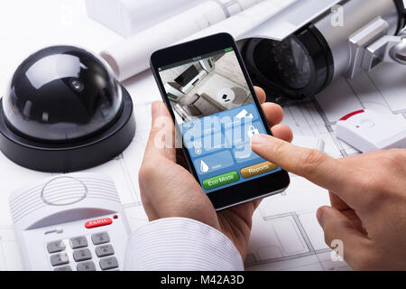 Person Hand Using Home Security System On Mobilephone With On Blueprint With Security Equipment Stock Photo