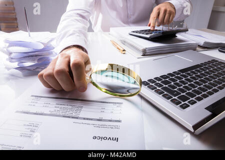 Midsection Of An Auditor Checking Invoice Using Magnifying Glass With Laptop And Documents On Desk Stock Photo
