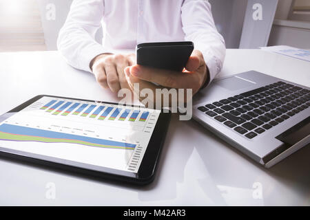 Close-up Of Digital Tablet Showing Graph Near Businessman Using Mobilephone On Desk Stock Photo