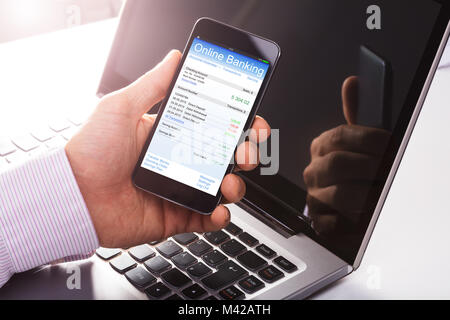 Close-up Of A Man Using Online Banking On Mobile Phone In Front Of Laptop Stock Photo