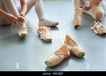 Ballet pointe shoes, blurred background. Ballerina putting on ballet slippers sitting on the floor. Footwear for ballet dancers.
